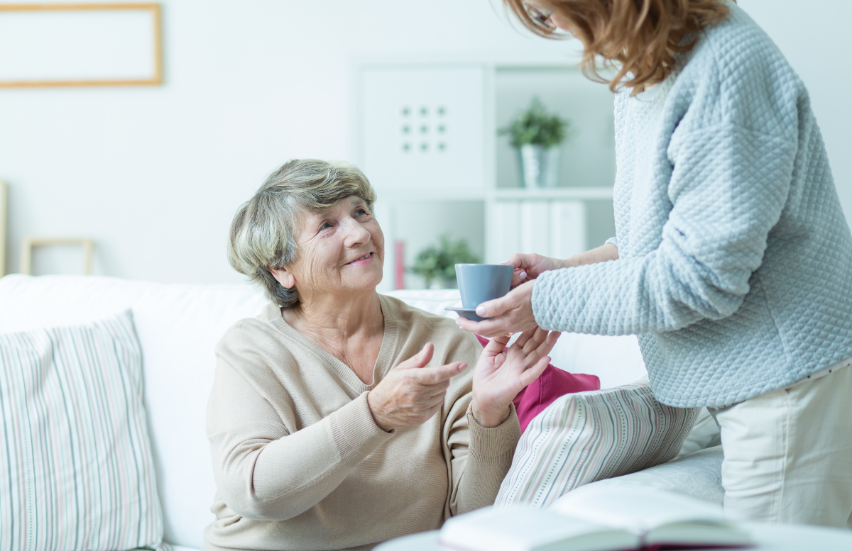 a-female-caregiver-offering-a-cup-of-tea-to-an-elderly-woman-in-person-centered-care-services