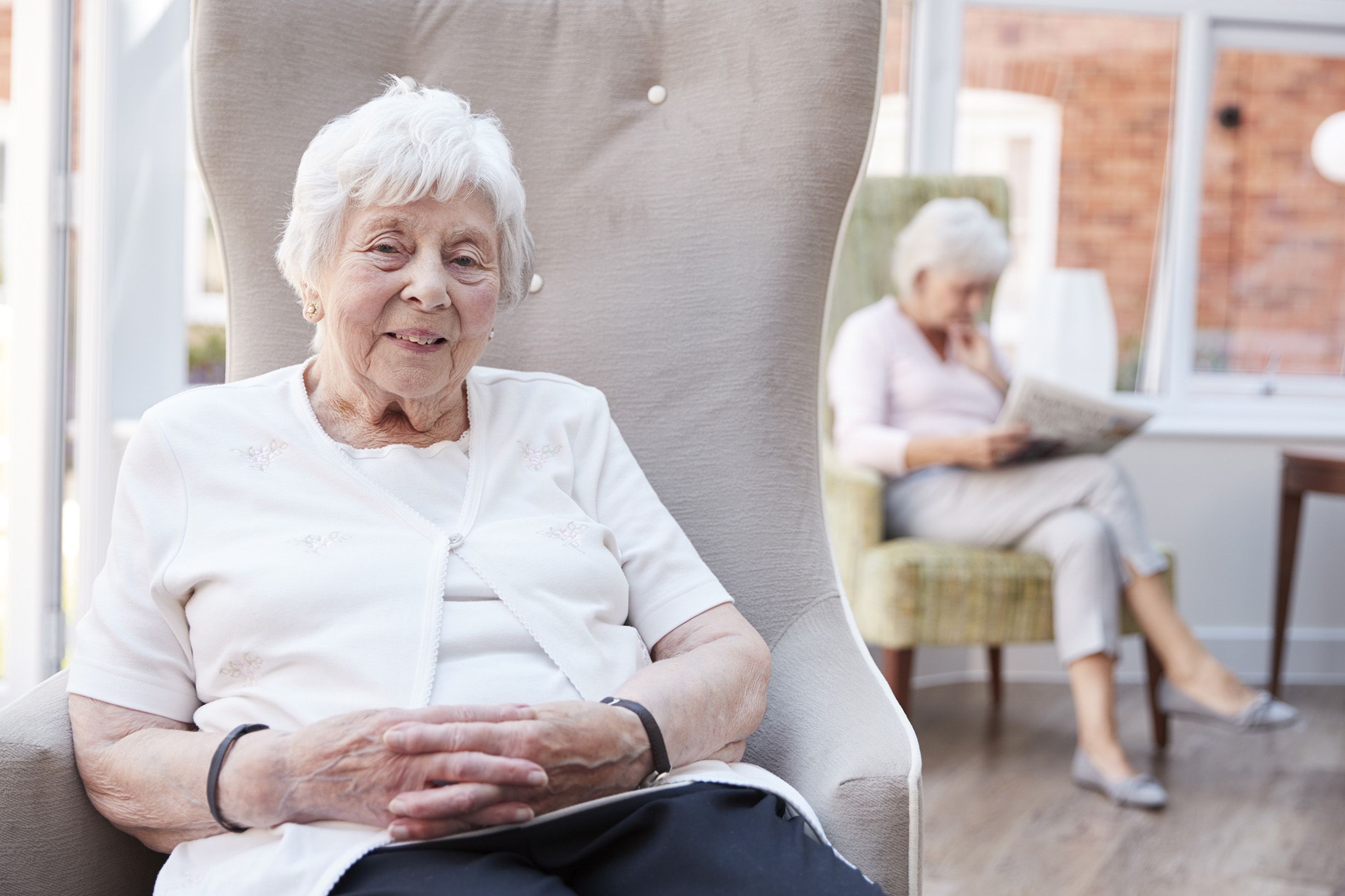 Portrait Of Senior Woman Sitting In Chair In Lounge Of Retirement Home