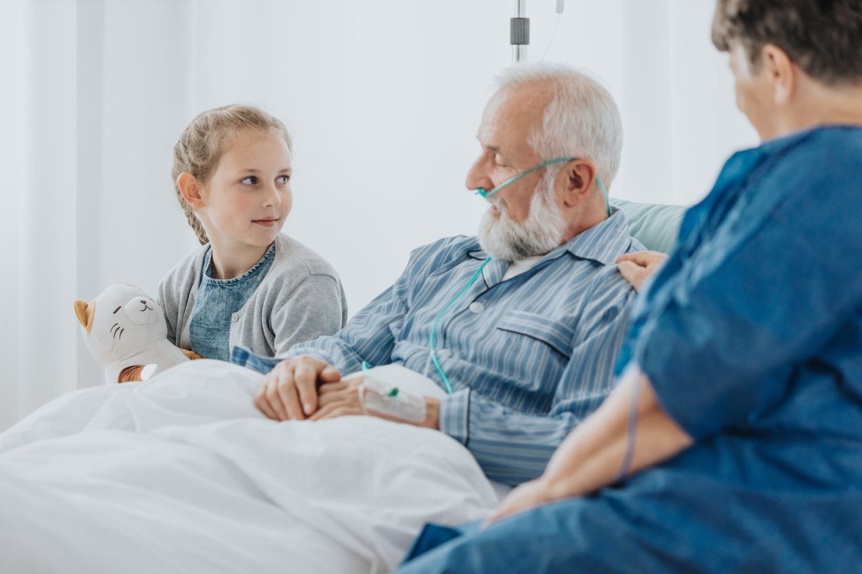 Advance care planning - An elderly male with an IV drip with his granddaughter and a caretaker at a hospital.